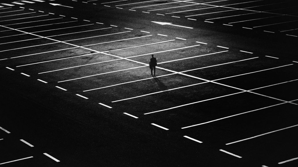 A person is walking in a dark empty parking lot