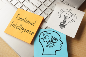 3 postit notes on top of a laptop, writing of Emotional Intelligence, drawing of light bulb and brain on them